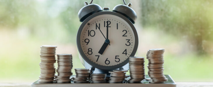 Alarm clock of coins stack and tablet on bokeh light nature background
