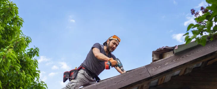 Man working on roof using electric screwdriver.